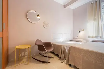 a bedroom with two beds and a chair and a mirror at ApartEasy - Plaza España & Fira in Barcelona