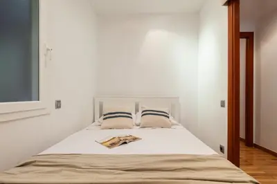 a white bedroom with a bed and a window at Flateli Paris in Barcelona
