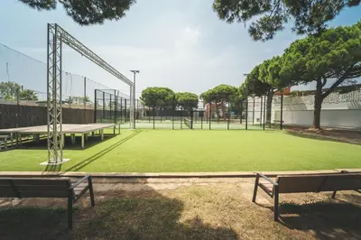 an empty tennis court with two benches on a field at Tres Estrellas Barcelona by HolaCamp in Gavà