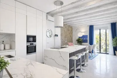 a kitchen with white marble countertops and a bar with stools at Colom Apartment 3BR with Balcony & Port Vell Views in Barcelona