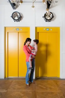 a woman holding a child in front of yellow doors at Praktik Bakery in Barcelona