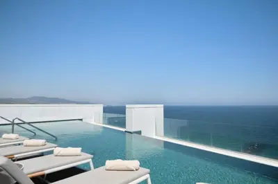 a swimming pool with lounge chairs and the ocean at Hotel Marina Badalona in Badalona