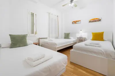 two beds in a white room with yellow and green pillows at Plaza Espanya Apartment in Barcelona