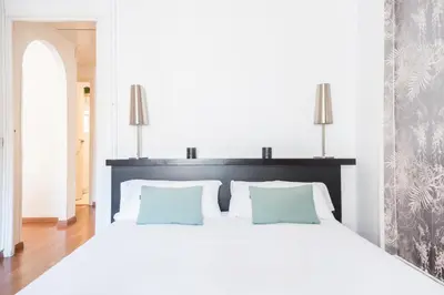 a white bedroom with a large white bed with blue pillows at Apartment with terrace a step away from Montjuic, Barcelona in Barcelona