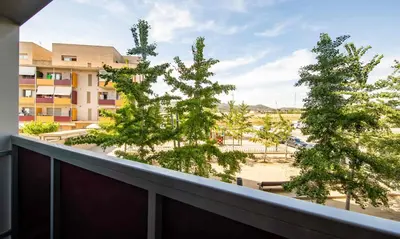 a balcony with two trees and a building at El Capricho Terrassa. in Terrassa