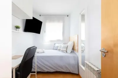 a white bedroom with a bed and a desk at El Capricho Terrassa. in Terrassa