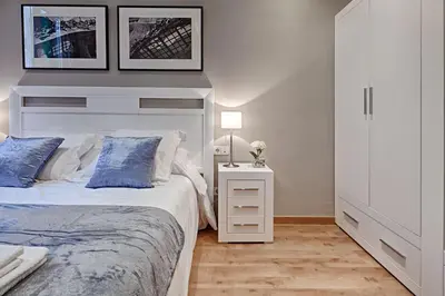 a white bedroom with a bed and a night stand at Habitat Apartments Batlló in Barcelona