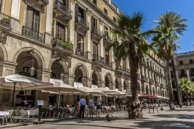 a building with tables and umbrellas and a palm tree at Habitat Apartments Ferran in Barcelona