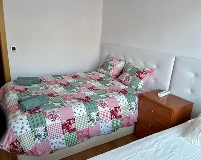 a bed with a red and green quilt and a night stand at Large Apartment near FIRA and City Center in Hospitalet de Llobregat
