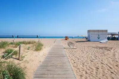 a wooden path on a beach with a bench at Apartamentos Balisse in Castelldefels