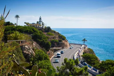 a road with a lighthouse on a hill next to the ocean at Vivalidays Apartour - Calella in Calella