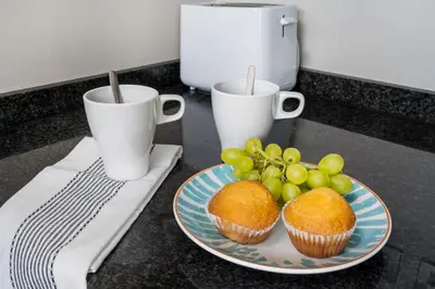 two cups and a plate of cupcakes and grapes on a counter at Lodging Apartments Forum Llull in Sant Adria de Besos