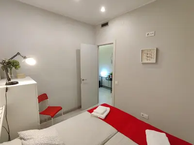 a white bedroom with a bed and a red chair at Fira Plaza España apartment in Barcelona