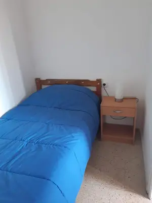 a bed with a blue comforter and a side table at Apartamentos Can bruguera 3 in Mataró