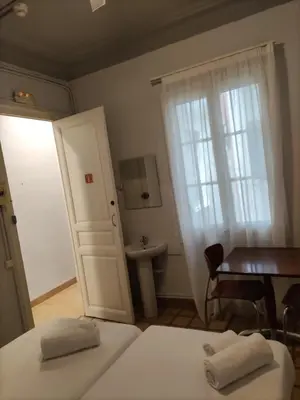 a bedroom with two beds and a table and a door at Hotel Monegal in Barcelona