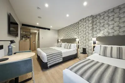 a hotel room with two beds and a desk at Catalonia Park Güell in Barcelona