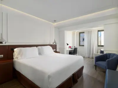 a bedroom with a large white bed and a blue chair at H10 Universitat in Barcelona