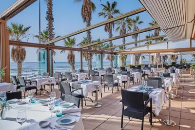 a restaurant with tables and chairs with the ocean in the background at Sunway Playa Golf & Spa Sitges in Sitges