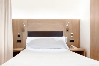 a bedroom with a white bed with a wooden headboard at Hotel Lleó in Barcelona