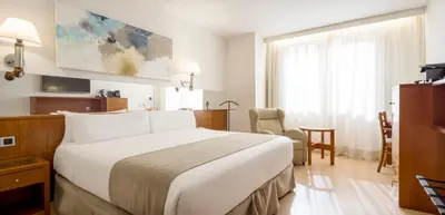 a hotel room with a large bed and a table at Ilunion Les Corts Spa in Barcelona