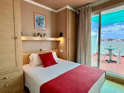 a bedroom with a bed and a balcony with a table at Hotel Piccadilly Sitges in Sitges