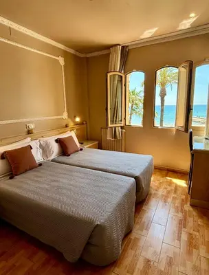 two beds in a hotel room with two windows at Hotel Celimar in Sitges