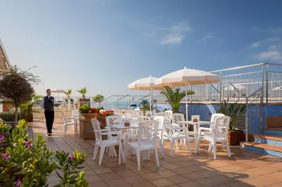 a man walking down a patio with white tables and chairs at htop Pineda Palace 4Sup - Adults Only #htopBliss in Pineda de Mar