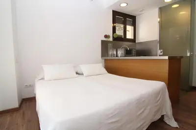 a bedroom with a white bed and a kitchen at BCN2STAY Apartments in Barcelona