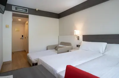 a hotel room with two beds and a red chair at Medplaya Hotel Santa Monica in Calella