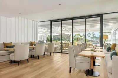 a restaurant with white chairs and tables and windows at Sabàtic Gavà Mar, Barcelona, a Tribute Portfolio Hotel in Gavà