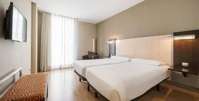 a bedroom with a large white bed and a chair at Ilunion Auditori in Barcelona