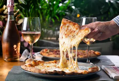 a person holding a slice of pizza on a table with wine glasses at AQUA Hotel Promenade & Spa 4Sup in Pineda de Mar