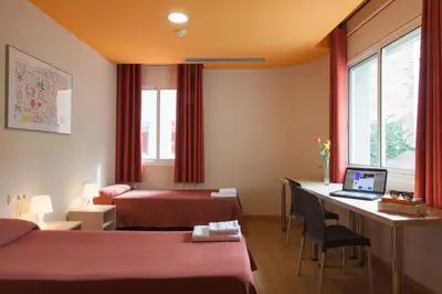a hotel room with two beds and a desk with a laptop at Residència Erasmus Gracia in Barcelona
