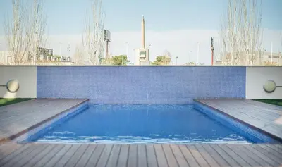 a swimming pool with a wooden deck and a brick wall at Large terrace luxury apartment in Sant Adria de Besos