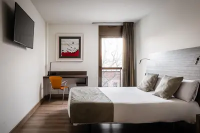 a bedroom with a bed and a desk and a window at Hotel HC*** Mollet Barcelona in Mollet del Vallès