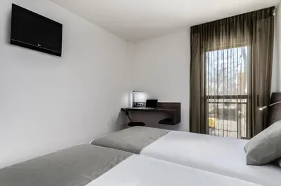 a white bedroom with a bed and a window at Hotel HC*** Mollet Barcelona in Mollet del Vallès