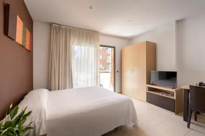 a bedroom with a white bed and a television at SG Costa BCN Apartments in Castelldefels