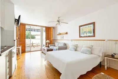 a bedroom with a white bed and a living room at Central - a 10 minutos de la paya in Sitges