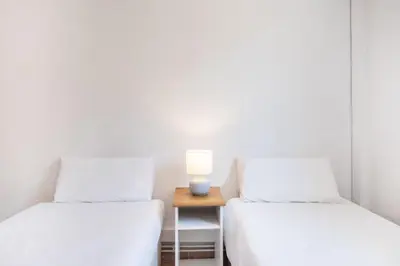 two beds in a room with a table with a lamp at Cozy Apt with charm and exquisite natural light in Barcelona