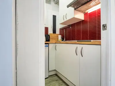 a kitchen with white cabinets and a red tiled wall at Pura Vida Apartment by Hello Homes Sitges in Sitges