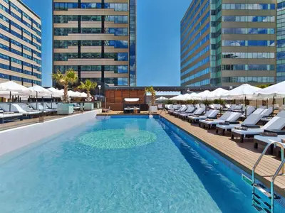 a swimming pool with chairs and umbrellas on a building at Hilton Diagonal Mar Barcelona in Barcelona
